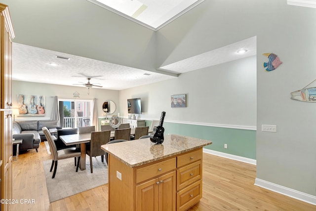 kitchen with ceiling fan, light stone countertops, light hardwood / wood-style floors, a textured ceiling, and a kitchen island