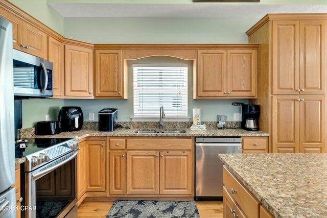 kitchen featuring light stone countertops, sink, stainless steel appliances, and light hardwood / wood-style flooring