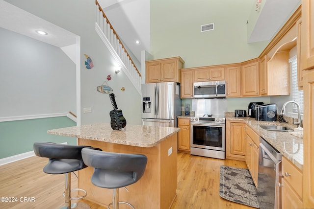 kitchen with sink, appliances with stainless steel finishes, a center island, light stone countertops, and light brown cabinets