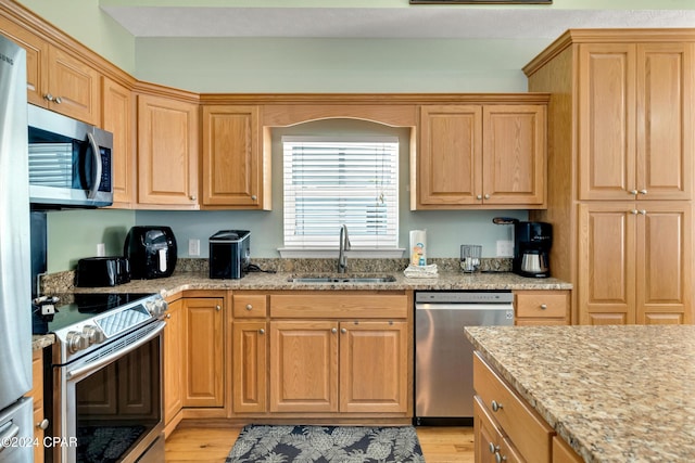 kitchen featuring stainless steel appliances, light stone countertops, sink, and light hardwood / wood-style floors