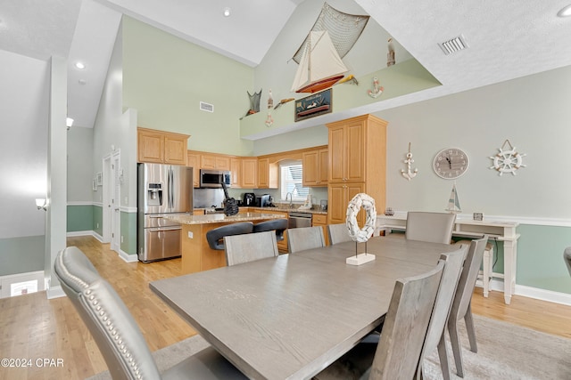 dining room featuring a textured ceiling, light hardwood / wood-style floors, high vaulted ceiling, and sink