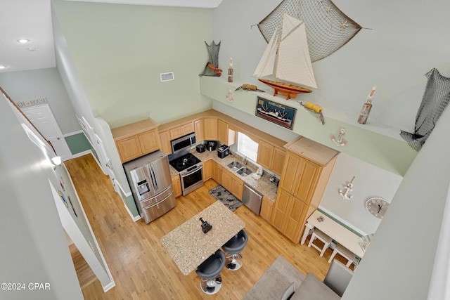 kitchen featuring light hardwood / wood-style flooring, stainless steel appliances, a high ceiling, and light brown cabinets