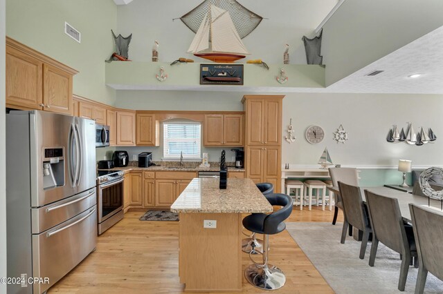 kitchen featuring light brown cabinetry, sink, a center island, stainless steel appliances, and light stone countertops