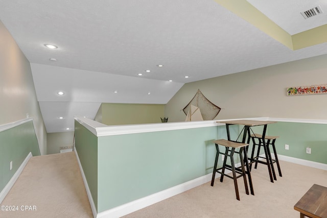 hallway with vaulted ceiling and light colored carpet