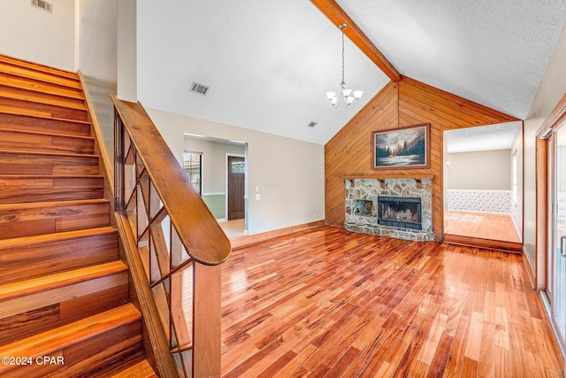 unfurnished living room with light wood-type flooring, wooden walls, high vaulted ceiling, a chandelier, and a stone fireplace