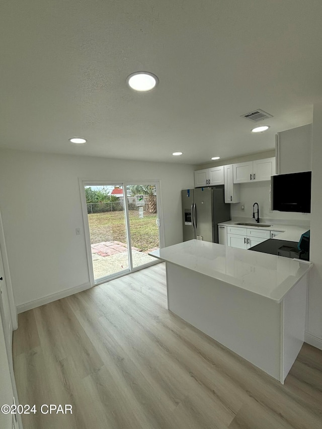 kitchen featuring kitchen peninsula, stainless steel refrigerator with ice dispenser, light wood-type flooring, light stone counters, and white cabinetry