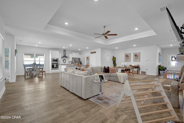 living room featuring ceiling fan, light hardwood / wood-style floors, a raised ceiling, and ornamental molding