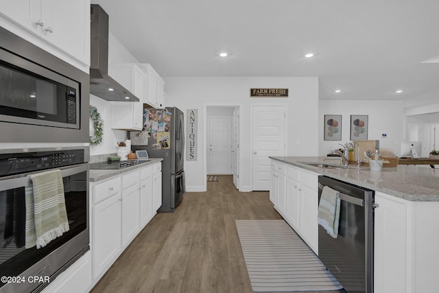 kitchen featuring sink, appliances with stainless steel finishes, an island with sink, wall chimney range hood, and white cabinets