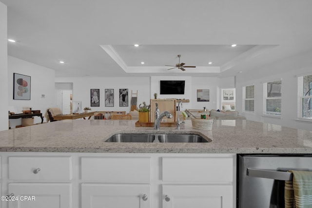 kitchen with light stone counters, a raised ceiling, sink, and dishwasher