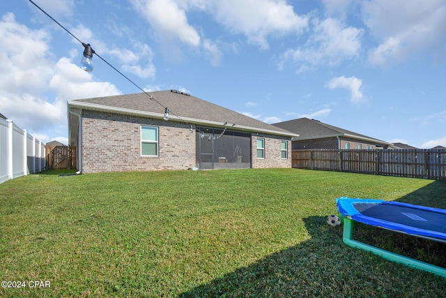 rear view of house featuring a trampoline and a lawn