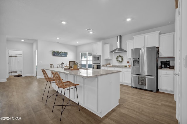 kitchen with white cabinetry, stainless steel appliances, wall chimney exhaust hood, and a center island with sink