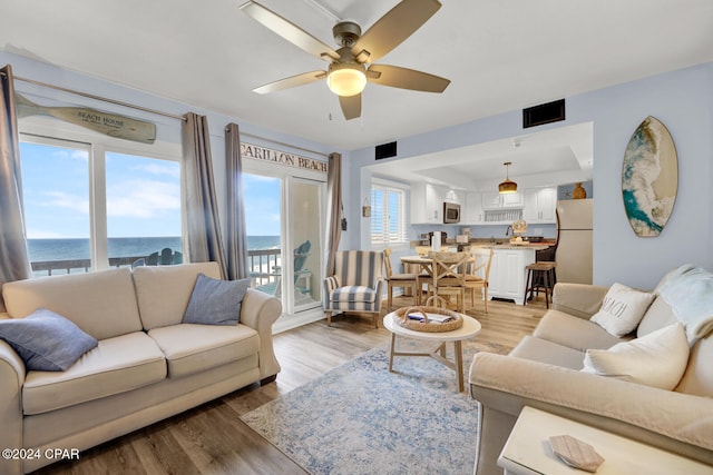 living room featuring ceiling fan, plenty of natural light, a water view, and hardwood / wood-style floors