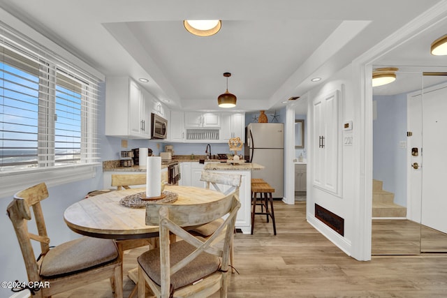 dining space featuring a tray ceiling, sink, and light hardwood / wood-style floors