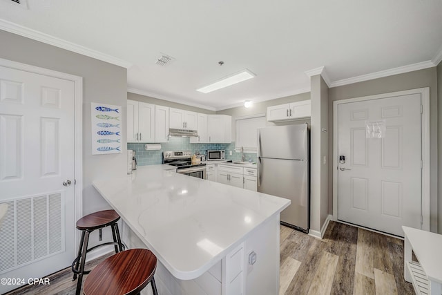 kitchen with a breakfast bar, white cabinetry, stainless steel appliances, and kitchen peninsula