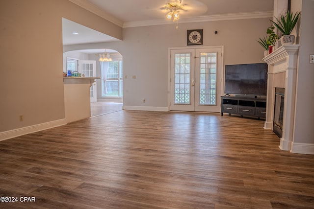 unfurnished living room with ornamental molding, ceiling fan with notable chandelier, french doors, and dark wood-type flooring