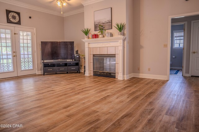 unfurnished living room featuring a tile fireplace, crown molding, french doors, and light wood-type flooring