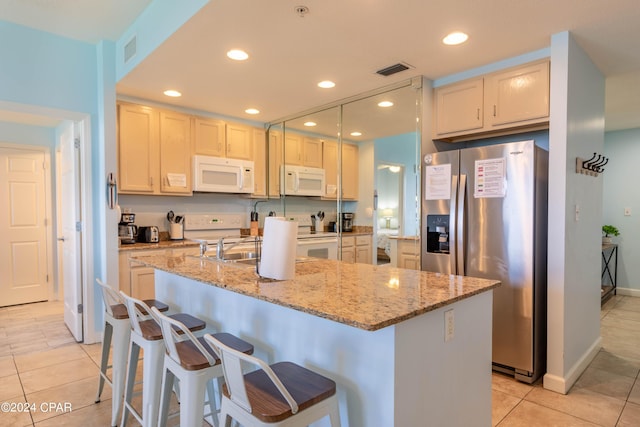 kitchen with white appliances, a kitchen bar, light stone countertops, and a kitchen island with sink