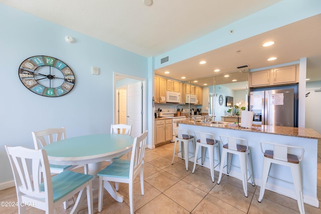 kitchen featuring a kitchen bar, light tile patterned floors, dark stone countertops, an island with sink, and white appliances