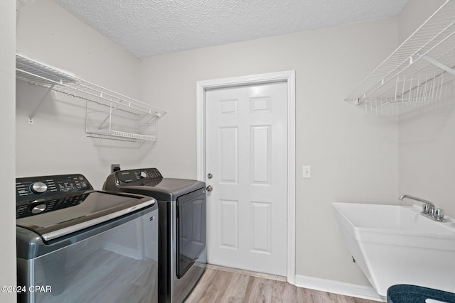 washroom with sink, a textured ceiling, light hardwood / wood-style floors, and washing machine and clothes dryer