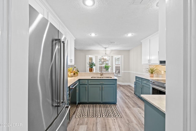 kitchen featuring white cabinetry, sink, light hardwood / wood-style floors, pendant lighting, and appliances with stainless steel finishes