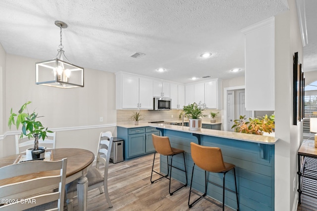 kitchen with blue cabinets, pendant lighting, light hardwood / wood-style floors, a breakfast bar area, and white cabinets