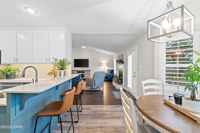 kitchen with a textured ceiling, pendant lighting, light hardwood / wood-style flooring, white cabinetry, and lofted ceiling