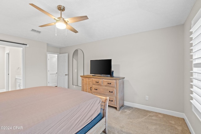 bedroom with a textured ceiling, ceiling fan, ensuite bathroom, and light carpet