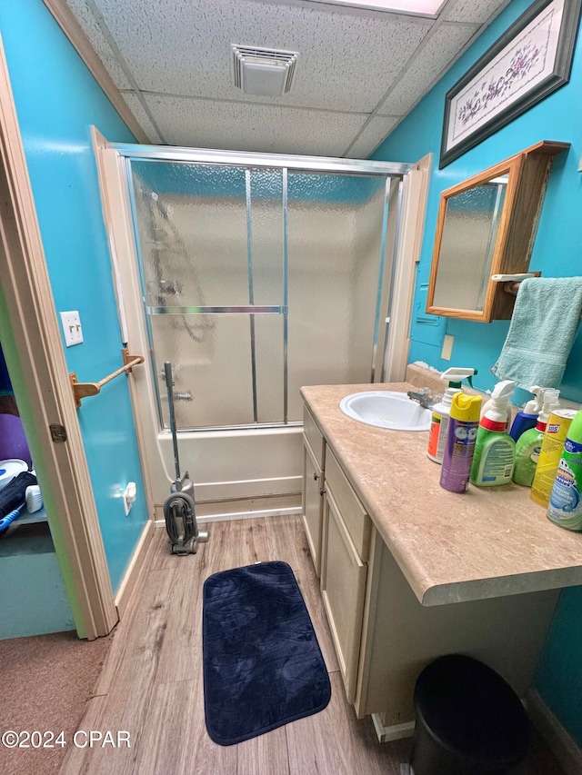 bathroom with hardwood / wood-style flooring, a drop ceiling, combined bath / shower with glass door, and vanity