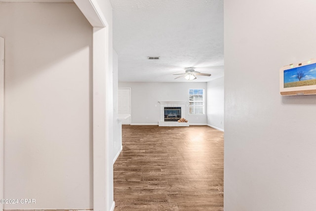 unfurnished living room with ceiling fan, a fireplace, wood-type flooring, and a textured ceiling