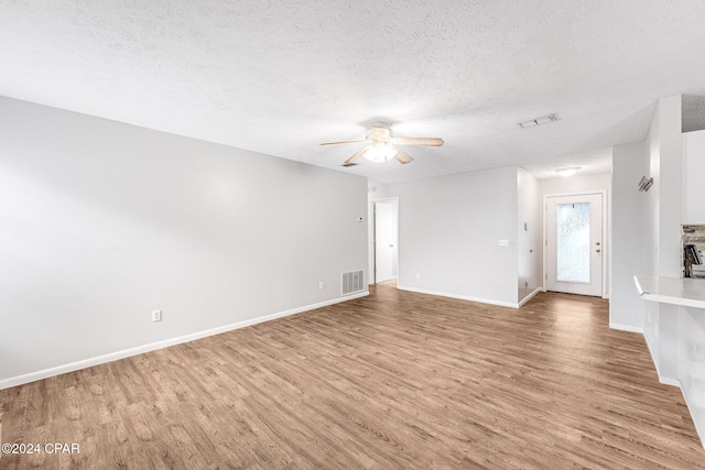 unfurnished living room featuring hardwood / wood-style flooring, ceiling fan, a fireplace, and a textured ceiling