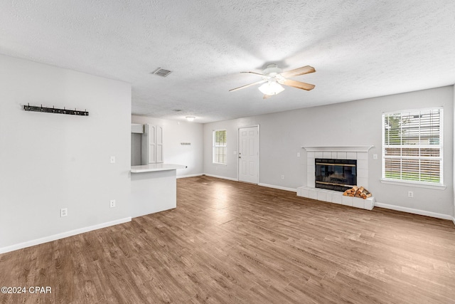 unfurnished living room featuring a textured ceiling, ceiling fan, wood-type flooring, and a fireplace