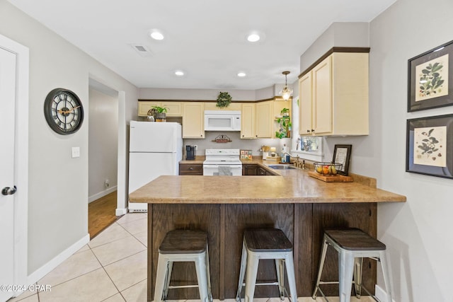 kitchen with white appliances, sink, light tile patterned flooring, a kitchen bar, and kitchen peninsula