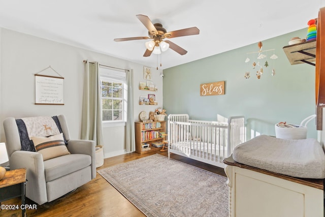 bedroom with hardwood / wood-style flooring, ceiling fan, and a nursery area