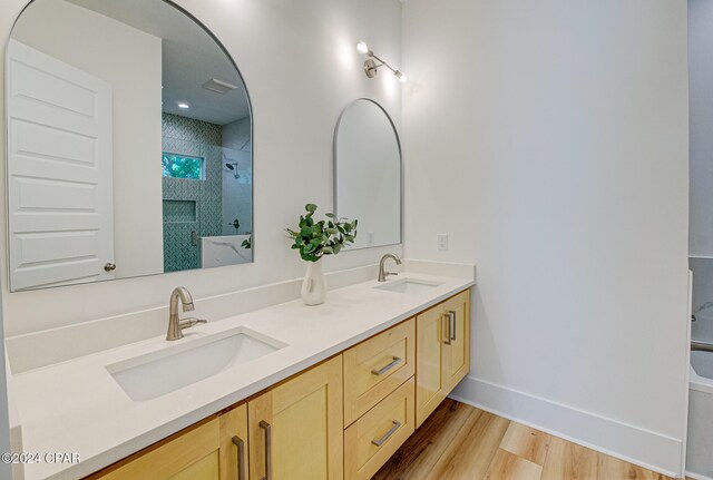 bathroom with hardwood / wood-style floors, vanity, and tiled shower