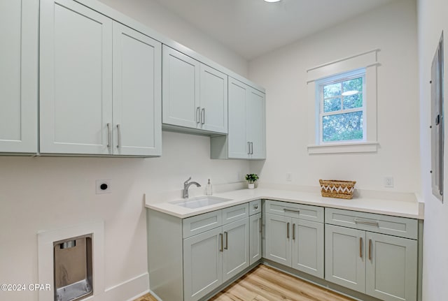 clothes washing area with cabinets, light wood-type flooring, electric dryer hookup, and sink