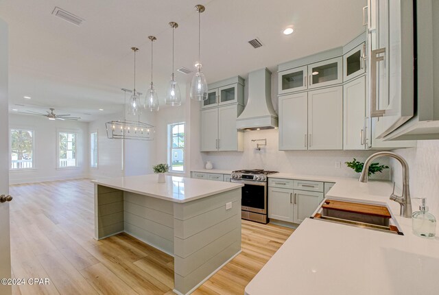 kitchen featuring custom range hood, ceiling fan, stainless steel gas stove, a kitchen island, and plenty of natural light