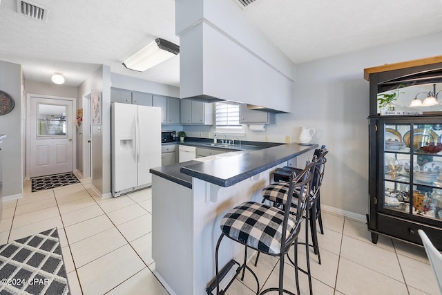 kitchen featuring white appliances, a kitchen breakfast bar, light tile patterned floors, a textured ceiling, and kitchen peninsula