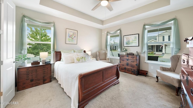 carpeted bedroom with a raised ceiling and a ceiling fan