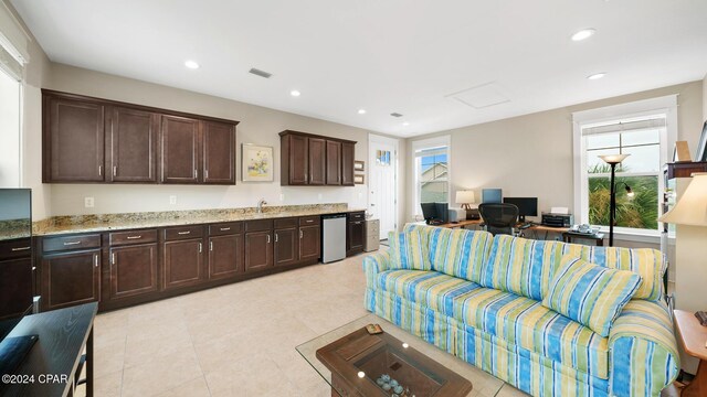 kitchen featuring recessed lighting, open floor plan, a sink, dark brown cabinets, and light stone countertops