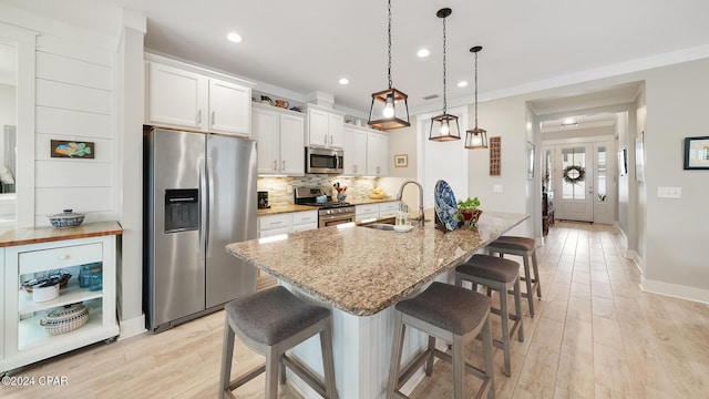 kitchen with a breakfast bar area, stainless steel appliances, tasteful backsplash, white cabinets, and a sink