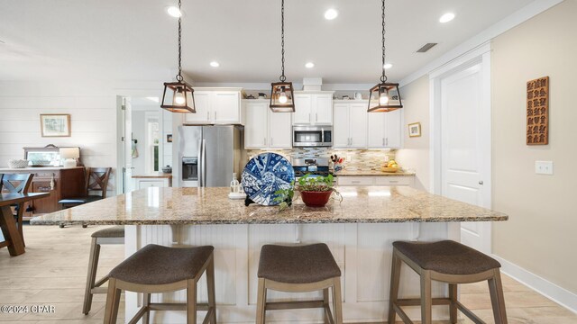 kitchen with a kitchen bar, light stone counters, stainless steel appliances, white cabinets, and a kitchen island