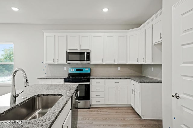 kitchen with stainless steel appliances, light stone countertops, sink, and white cabinets