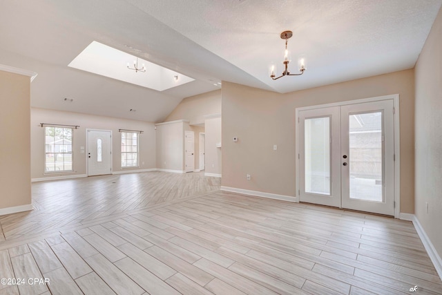 interior space with french doors, light hardwood / wood-style floors, a notable chandelier, and vaulted ceiling with skylight