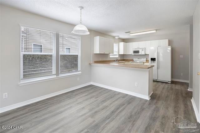 kitchen with white appliances, kitchen peninsula, hanging light fixtures, dark hardwood / wood-style floors, and white cabinetry