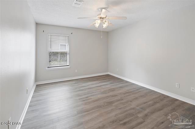 empty room with a textured ceiling, ceiling fan, and dark hardwood / wood-style floors