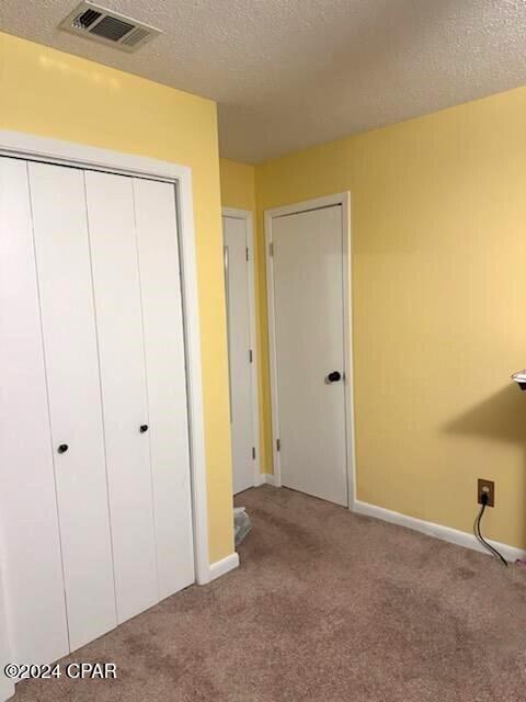 unfurnished bedroom featuring carpet, visible vents, and a textured ceiling