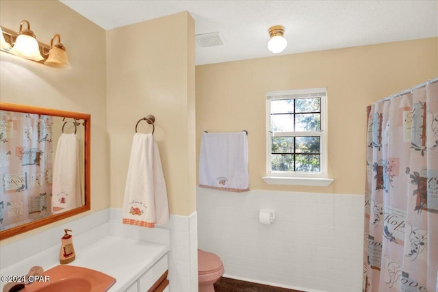 full bath with visible vents, wainscoting, toilet, vanity, and tile walls