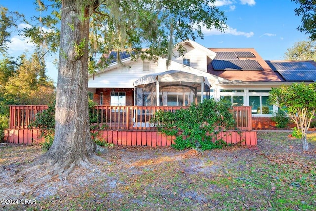 view of front of home with roof mounted solar panels, a deck, and brick siding