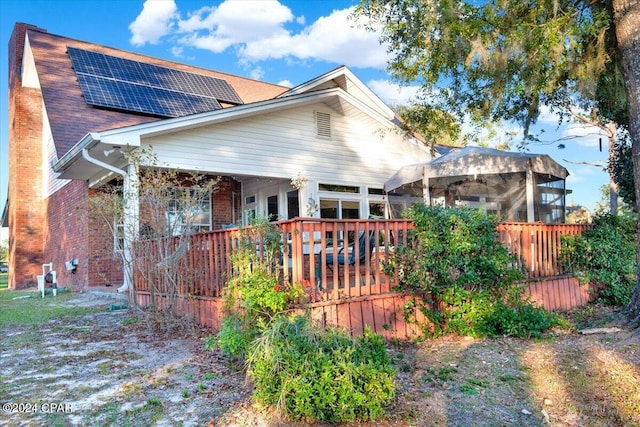 view of front of house with a gazebo, brick siding, a shingled roof, and roof mounted solar panels