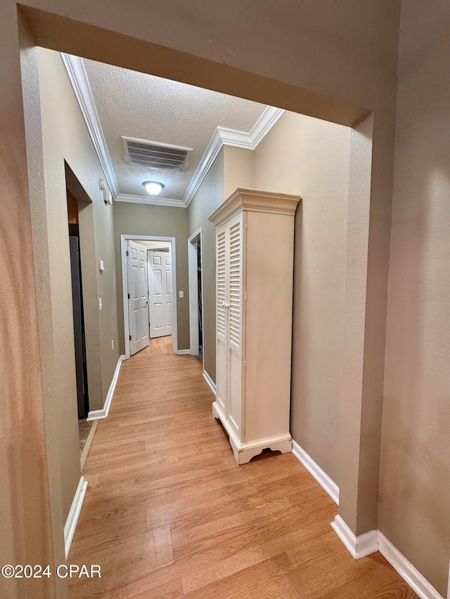 hallway featuring light hardwood / wood-style floors, ornamental molding, and a textured ceiling